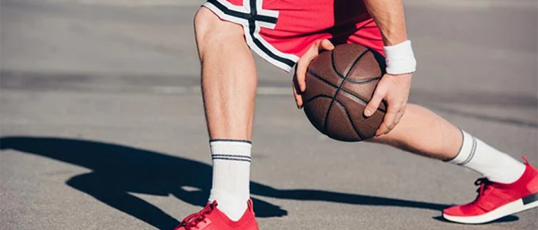 Баскетболист переводит мяч под ногой, делает финт